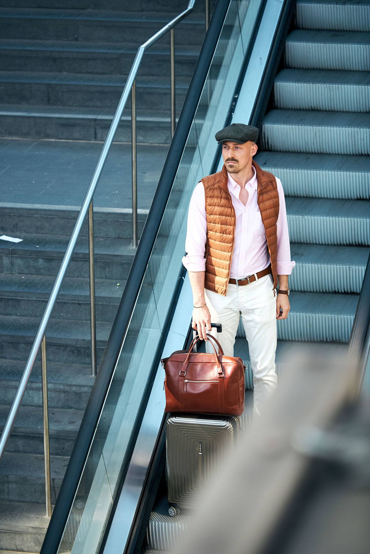 junger Mann mit Schirmmütze und Business Outfit auf einer Rolltreppe